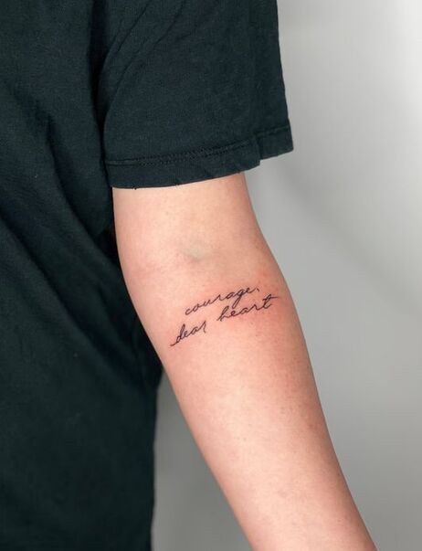 Photo of Ellery Hall's left arm. She wears a black t-shirt. A script tattoo under her elbow reads, 