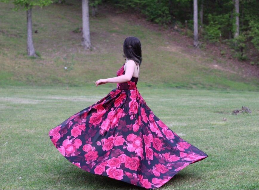 Ellery Hall wearing a black and red floral prom dress, spinning in the grass.